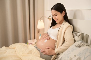 Güzel hamile bir kadın nemlendirici sürüyor, göbeğinde gerilme izi kremi, kısırlık tedavisi, tüp bebek, gelecekteki annelik konsepti.