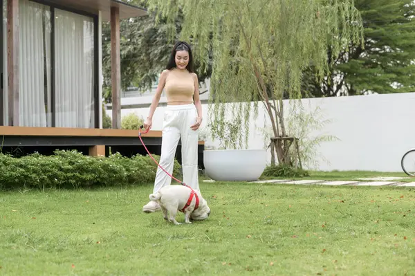 Mutlu Asyalı kadın arka bahçede sevimli akıllı köpek yavrusuyla oynuyor.