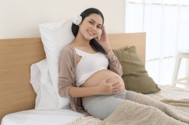 Kulaklıklı mutlu hamile kadın Mozart müzik dinliyor ve yatakta uzanıyor, hamilelik kavramı.