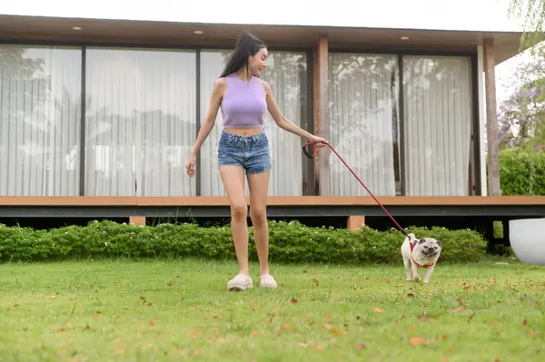 Mutlu Asyalı kadın arka bahçede sevimli akıllı köpek yavrusuyla oynuyor.