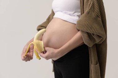 Beyaz arka plan stüdyosu, sağlık ve annelik konsepti üzerinde muz tutan güzel hamile kadın portresi