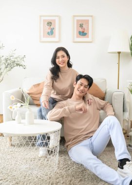 Evdeki oturma odasında oturan Asyalı genç çiftin portresi.