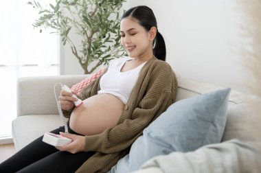 Hamile kadın, bebeğin kalp atışlarını dinlemek için cep bebeği doppler kullanıyor. 