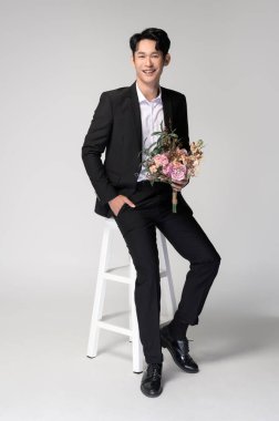 Damat beyaz arka planda düğün buketi tutuyor. 