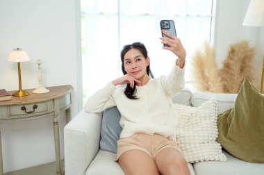 Genç Asyalı kadın evdeki oturma odasında akıllı telefon kullanmaktan hoşlanıyor.