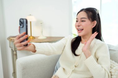 Genç Asyalı kadın evdeki oturma odasında akıllı telefon kullanmaktan hoşlanıyor.