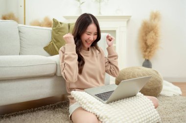 Genç Asyalı kadın oturma odasında dizüstü bilgisayar kullanmaktan hoşlanıyor.