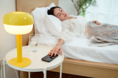 Uyuyan Asyalı kadın sabah uyandığında akıllı telefondan alarmı kapatıyor.