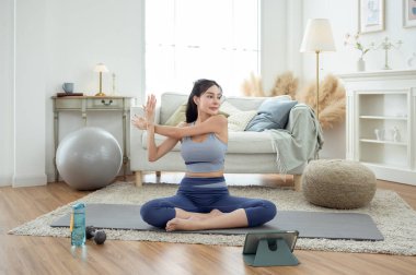 Spor giyimli Asyalı bir kadın evde yoga yapıyor ve egzersiz yapıyor.