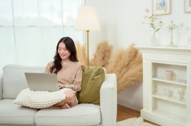 Genç Asyalı kadın oturma odasında dizüstü bilgisayar kullanmaktan hoşlanıyor.