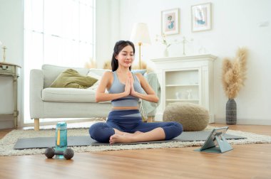 Spor giyimli Asyalı bir kadın evde yoga yapıyor ve egzersiz yapıyor.