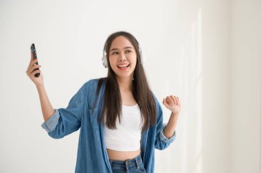 Genç Asyalı bir kadın müzik dinlemekten ve beyaz arka planda dans etmekten hoşlanıyor. 