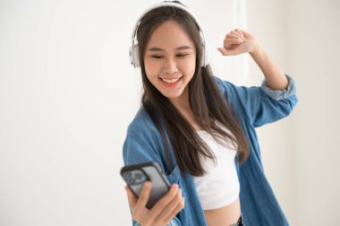 Genç Asyalı bir kadın müzik dinlemekten ve beyaz arka planda dans etmekten hoşlanıyor. 