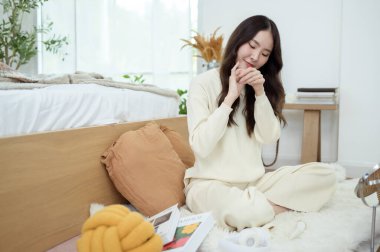 Genç Asyalı kadın evde krem nemlendirici sürüyor.