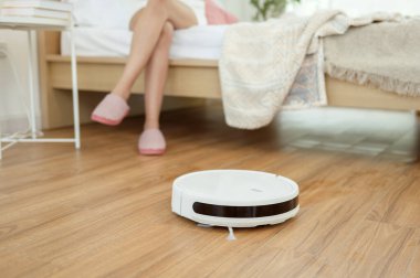 Robotik elektrikli süpürge çalışırken Asyalı genç kadın dinleniyor.