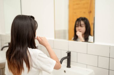 Genç bir kadın tuvalette dişlerini fırçalıyor.