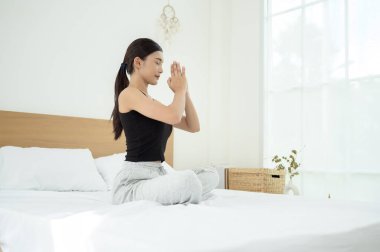 Genç Asyalı kadın yatak odasında meditasyon yapıyor.