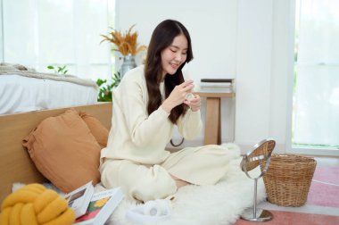 Genç Asyalı kadın evde krem nemlendirici sürüyor.