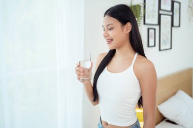 Genç Asyalı kadın evde su içiyor.
