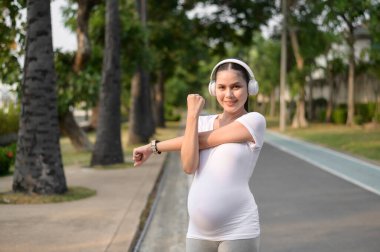 Güzel hamile kadın parkta egzersiz yapıyor ve esniyor.