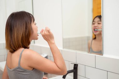 Genç bir kadın tuvalette dişlerini fırçalıyor.