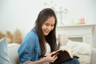 Genç Asyalı kadın oturma odasında kitap okumaktan zevk alıyor.