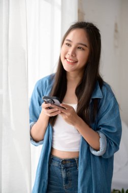 Genç Asyalı kadın evde akıllı telefon kullanmaktan hoşlanıyor.