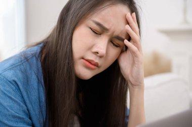 Genç Asyalı kadın evdeki oturma odasında stres hissediyor.