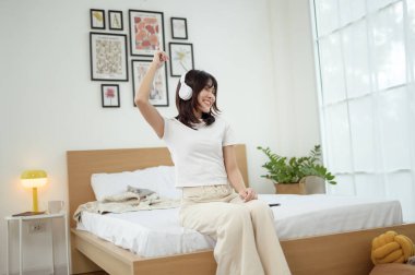 Çiçeklerle dolu, modern, aydınlık bir yatak odasında kadın gülümser ve yatakta dans eder..