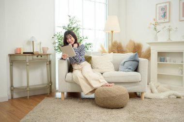 Kadın koltukta dinleniyor, parlak, davetkar bir yerde tabletle meşgul..