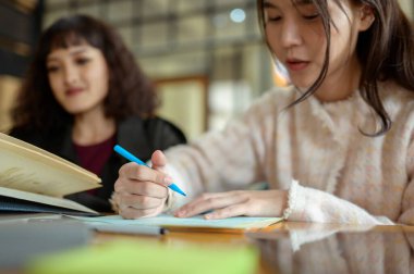 İki arkadaş rahat bir kafe masasında okul ödevlerinde işbirliği yapıyor, fikirleri ve materyalleri paylaşıyorlar..