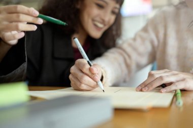 İki arkadaş rahat bir kafe masasında okul ödevlerinde işbirliği yapıyor, fikirleri ve materyalleri paylaşıyorlar..