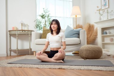 Bir kadın, davet ettiği oturma odasında yoga minderinde yan esneme hareketi yapıyor..