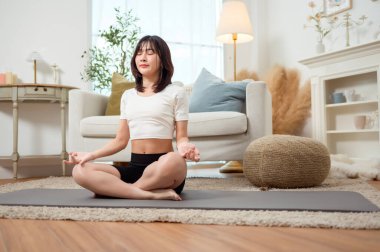 Bir kadın, davet ettiği oturma odasında yoga minderinde yan esneme hareketi yapıyor..