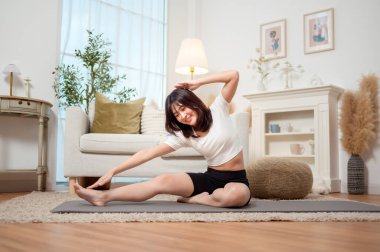 Bir kadın, davet ettiği oturma odasında yoga minderinde yan esneme hareketi yapıyor..