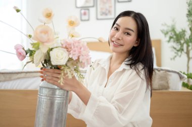 Asyalı gülümseyen kadın kavanoza güzel çiçekler koyuyor