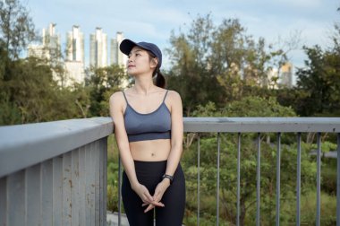 Kadın sıcak güneşin ve şehrin siluetinin tadını çıkarırken tırabzanda dinleniyor..