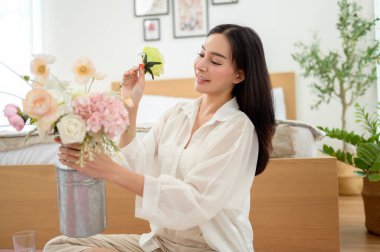 Asyalı gülümseyen kadın kavanoza güzel çiçekler koyuyor