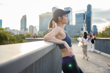 Kadın sıcak güneşin ve şehrin siluetinin tadını çıkarırken tırabzanda dinleniyor..