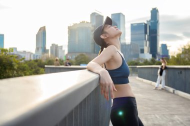 Kadın sıcak güneşin ve şehrin siluetinin tadını çıkarırken tırabzanda dinleniyor..