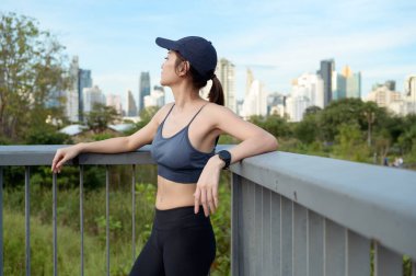 Kadın sıcak güneşin ve şehrin siluetinin tadını çıkarırken tırabzanda dinleniyor..