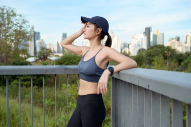 Kadın sıcak güneşin ve şehrin siluetinin tadını çıkarırken tırabzanda dinleniyor..