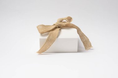 Düzgün paketlenmiş bir hediye kutusu arka planda duruyor, çuval bezi kurdelesiyle süslenmiş..