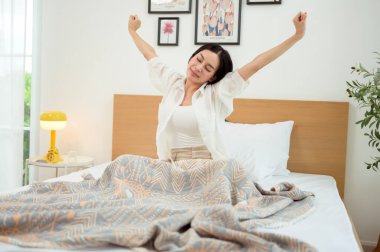 Genç Asyalı kadın sabah uyandıktan sonra yatakta geriniyor.