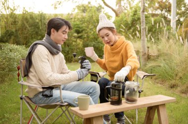 İki arkadaş bahçede dinlenir, sıcak içkilerini yudumlar ve güneşli bir günde sohbet ederler..