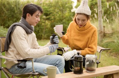 İki arkadaş bahçede dinlenir, sıcak içkilerini yudumlar ve güneşli bir günde sohbet ederler..