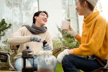 İki arkadaş bahçede dinlenir, sıcak içkilerini yudumlar ve güneşli bir günde sohbet ederler..