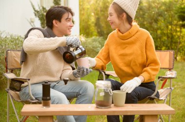 İki arkadaş bahçede dinlenir, sıcak içkilerini yudumlar ve güneşli bir günde sohbet ederler..