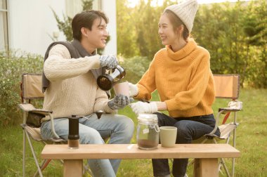 İki arkadaş bahçede dinlenir, sıcak içkilerini yudumlar ve güneşli bir günde sohbet ederler..