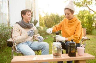 İki arkadaş bahçede dinlenir, sıcak içkilerini yudumlar ve güneşli bir günde sohbet ederler..